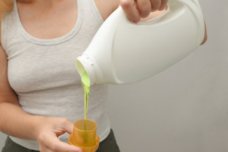 Woman pours liquid washing gel into plastic cap. Concept of washing clothes, domestic routine and household chores. Close up of attractive female pouring liquid green gel into bottle cap.の写真素材