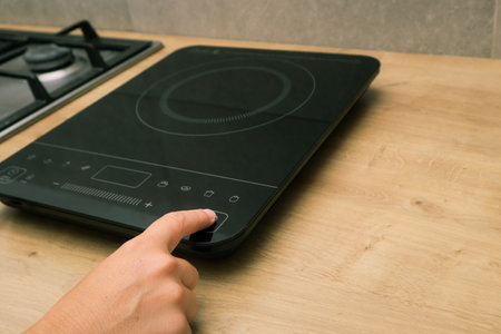 Woman hand turn on induction stove. Finger touching sensor button on induction or electrical hob. Induction cooktop. Switching on the burner cooktop.の写真素材