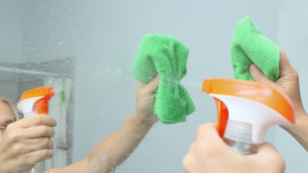 cleaning service. Cleaning and polish mirror with rag and spray in bathroom at home. Woman cleaning...