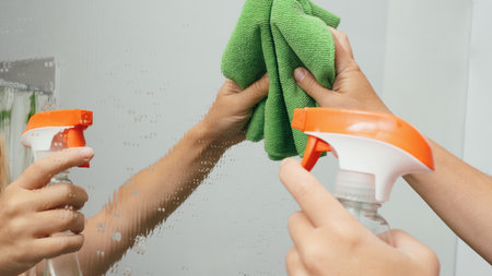 cleaning service. Cleaning and polish mirror with rag and spray in bathroom at home. Woman cleaning a bathroom's mirror with sanitizing spray and sponge.の写真素材