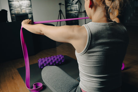 Fit young woman with exercise rubber bands for fitness and foam massage roller for myofascial release. Female athlete exercising with resistance band on gray mat. Healthy lifestyle, fitness concept.の写真素材