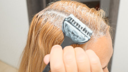 Woman dyeing her hair in front of mirror at home. Closeup woman hands dyeing hair using a black brush.の写真素材