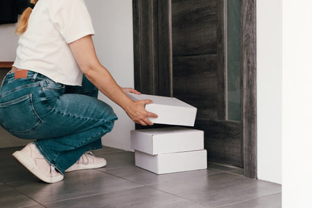Woman opens door to get delivery from porch. Woman in casual jeans clothes collects parcel at front...