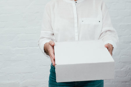 Woman giving parcel on white background. Delivery, relocation and unpacking. Woman hands with cardboard box. Unrecognizable woman holding box.の写真素材