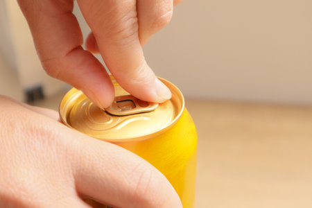 A woman's hand opening an aluminum yellow beer or soda. Close up. Selective focus on a hand with a...