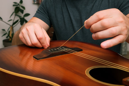 Man changing the strings of a guitar at home. Hands of a young man changing the string on an...