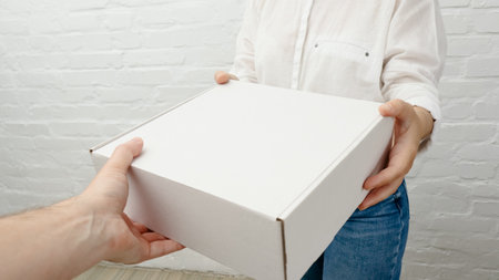 Young woman receiving parcel from delivery man, white brick background. Black Friday sale. Online shopping.の写真素材