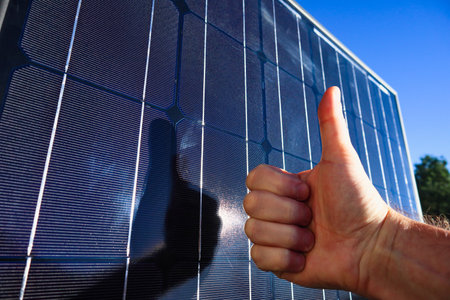 Hand showing thumbs up by the backdrop is solar energy. Concept of clean solar energy. Like to alternative energy sun energy power. Electric power engineer thumbs up against solar panelsの写真素材