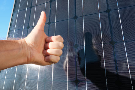 Hand showing thumbs up by the backdrop is solar energy. Concept of clean solar energy. Like to alternative energy sun energy power. Electric power engineer thumbs up against solar panelsの写真素材