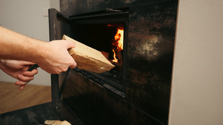 Heating home concept. Mans hand loading firewood into burning fireplace. Solid fuel and heating conceptの写真素材