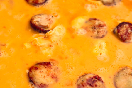 Cooking omelette with sausage. Liquid egg for scrambled eggs with is being poured into frying pan.の写真素材