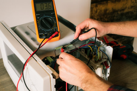 A repair engineer uses a multimeter to check the circuits of a microwave oven, looking for a fault....