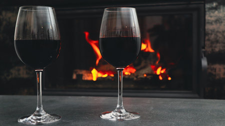 Two glasses of red wine on a background of a burning fireplace. Romantic evening near the fireplaceの写真素材