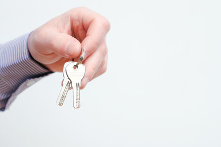 Hand holding house keys. Moving house, relocation. Caucasian male hand holding key to house on white background. Human hand holds the key from new house. Copy spaceの写真素材