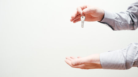 Hand holding house keys. Moving house, relocation. Caucasian male hand holding key to house on white background. Human hand holds the key from new house. Copy spaceの写真素材