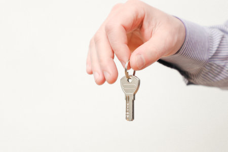 Hand holding house keys. Moving house, relocation. Caucasian male hand holding key to house on white background. Human hand holds the key from new house. Copy spaceの写真素材