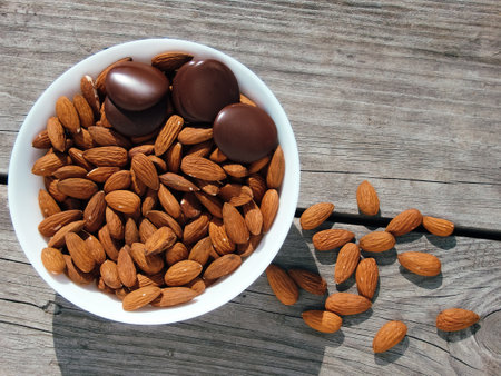 Almonds and dark chocolate in a bowl on a wooden table. Healthy snack. space for text and close up. Bowl with tasty chocolate and almonds on gray old table.の写真素材