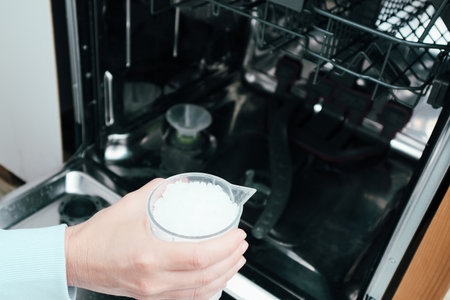 A woman pours industrial salt into the dishwasher. A woman adds salt for dishwasher descaling or water softening.の写真素材