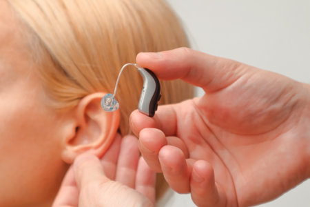 The hands of a male audiologist trying on a hearing aid on a woman's ear. Helping technologies for people with disabilities, closeupの写真素材