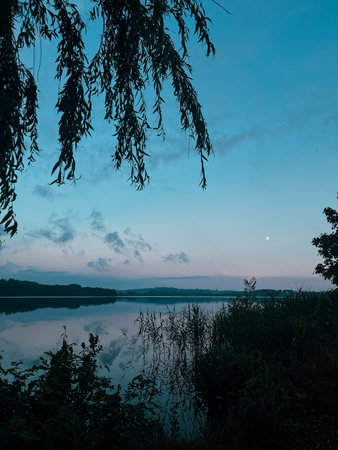 Quiet lake surface, very peaceful, no people, lake reflection background. Beautiful view of the lake shore with trees at sunset. Lake with gray clouds at sunset.の写真素材