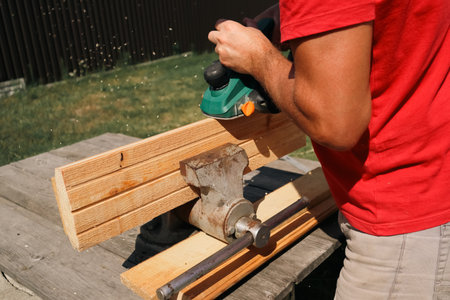 A carpenter planes a piece of wood using an electric plane. Carpenter is planning a wooden plank....