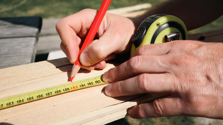 A carpenter marks a piece of wood with a tape measure and pencil. Measuring plank of wood and marking with pencil. Builder, repairman makes pencil marks.の写真素材