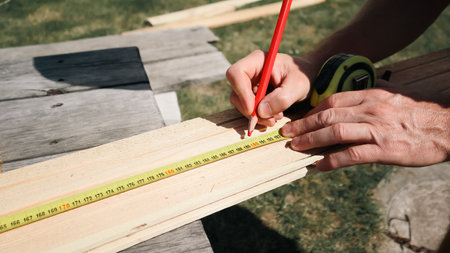 A carpenter marks a piece of wood with a tape measure and pencil. Measuring plank of wood and marking with pencil. Builder, repairman makes pencil marks.の写真素材