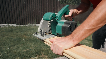 Carpenter sawing wood with handsaw. Carpenter working with a circular saw outside in sunny day. Wood chips flying.の写真素材