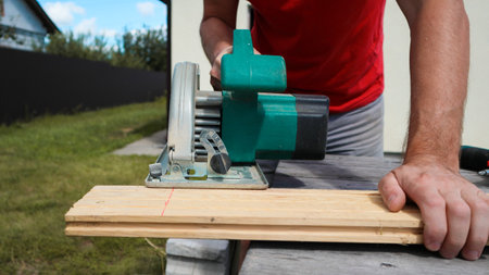 Carpenter sawing wood with handsaw. Carpenter working with a circular saw outside in sunny day. Wood chips flying.の写真素材