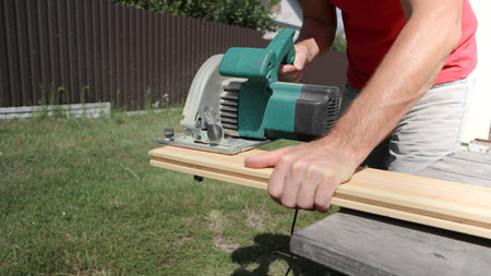 Carpenter sawing wood with handsaw. Carpenter working with a circular saw outside in sunny day. Wood chips flying.の写真素材