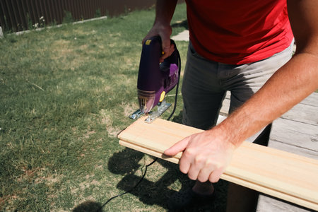Carpenter installing decking boards. Carpenter building wooden deck outside workshop. Construction...