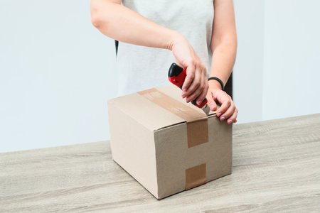 Woman Opens Box. A woman opening a carboard box container delivery. Woman unboxing cardboard box with knifeの写真素材