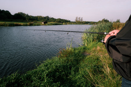 Trout fishing with spinning rod on a small lake. Fisherman fishing in a lake. Close-up of fishing rod on lakeの写真素材