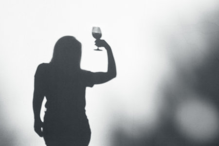 Woman celebrating with wine. Silhouetted shadow of woman with glass of wine. Silhouette of female holding wineの写真素材