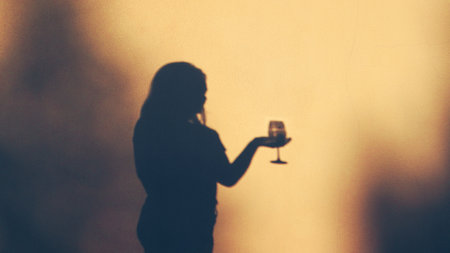 Woman celebrating with wine. Silhouetted shadow of woman with glass of wine. Silhouette of female holding wineの写真素材