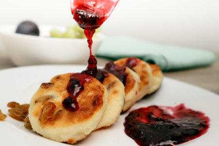 Female hand with spoon with jam preparing cheese pie. Blueberry jam on cheesecake. Cheese cake cooking - topping with strawberry jamの写真素材