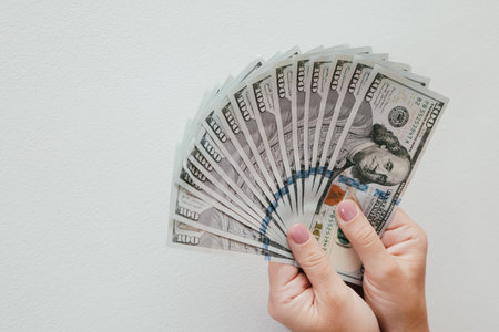 woman hands holding us dollar bills. Woman's hands shows a fan of money on white background.の写真素材