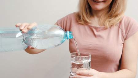 Pouring water from blue plastic bottle in glass. Banner with concept of natural clean aqua at home.の写真素材