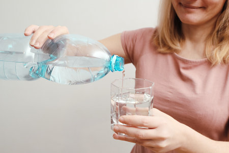 Pouring mineral water from blue plastic bottle in glass. Banner with concept of natural clean aqua at home.の写真素材