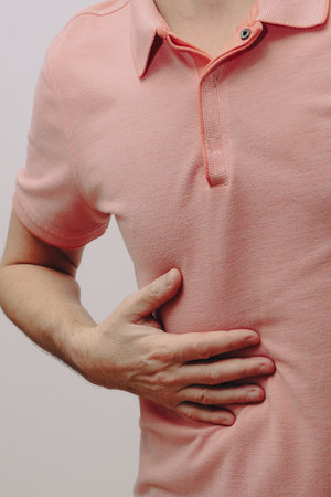 Man in pain holding his hurting stomach rubbing his right side. Young Man With Stomach Problems. Young man having medical issuesの写真素材