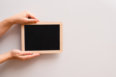 Woman's hand showing chalkboard. Place for writing text on a blackboard. Hands Holding a Blank Chalkboard Frame.の写真素材