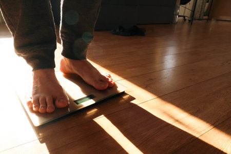 Person measuring their weight using scales on floor. Weight loss. Shadow on a sunny morning.の写真素材