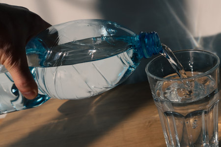 Man pouring mineral water from plastic bottle in glass. Male hand pour water in glass from bottleの写真素材