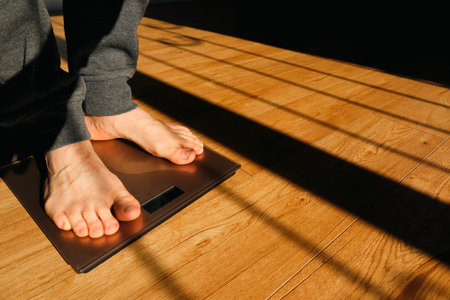 Person measuring their weight using scales on floor. Weight loss. Shadow on a sunny morning.の写真素材