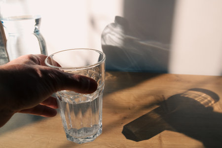 Hand holding drinking water bottle pouring into glass. Pouring water from a plastic bottle into a glass. Sun shadows.の写真素材