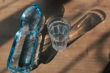 Mineral water blue plastic bottle in glass, with sunlight deep shadow of glass. Hard sunlight. Water...