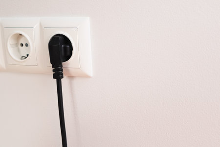 An electrical socket in the wall in the apartment of the house. Black power cord cable plugged into European wall outlet. Plug with socket. Connection. Electricity.の写真素材