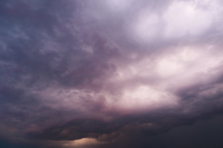Dramatic thunderstorm with dark clouds in the evening. Dramatic sky of clouds reflecting strong hues of orange, pink, blue and yellow lighting upの写真素材