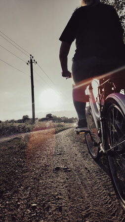 Woman riding cruiser bike on bicycle path at sunset. Back view. Cyclist girl biker enjoys freedom, healthy lifestyle. Outdoor sport activity. Active summer holidays.の写真素材