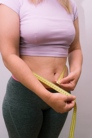 Unrecognizable lady checking result of weight loss diet or liposuction. Overweight woman measuring...